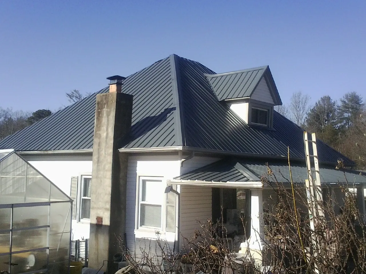 Dark blue standing seam metal roof on a white farmhouse with dormer — Slate & Tile Roof Repair by Roofing Brothers in Sturgis