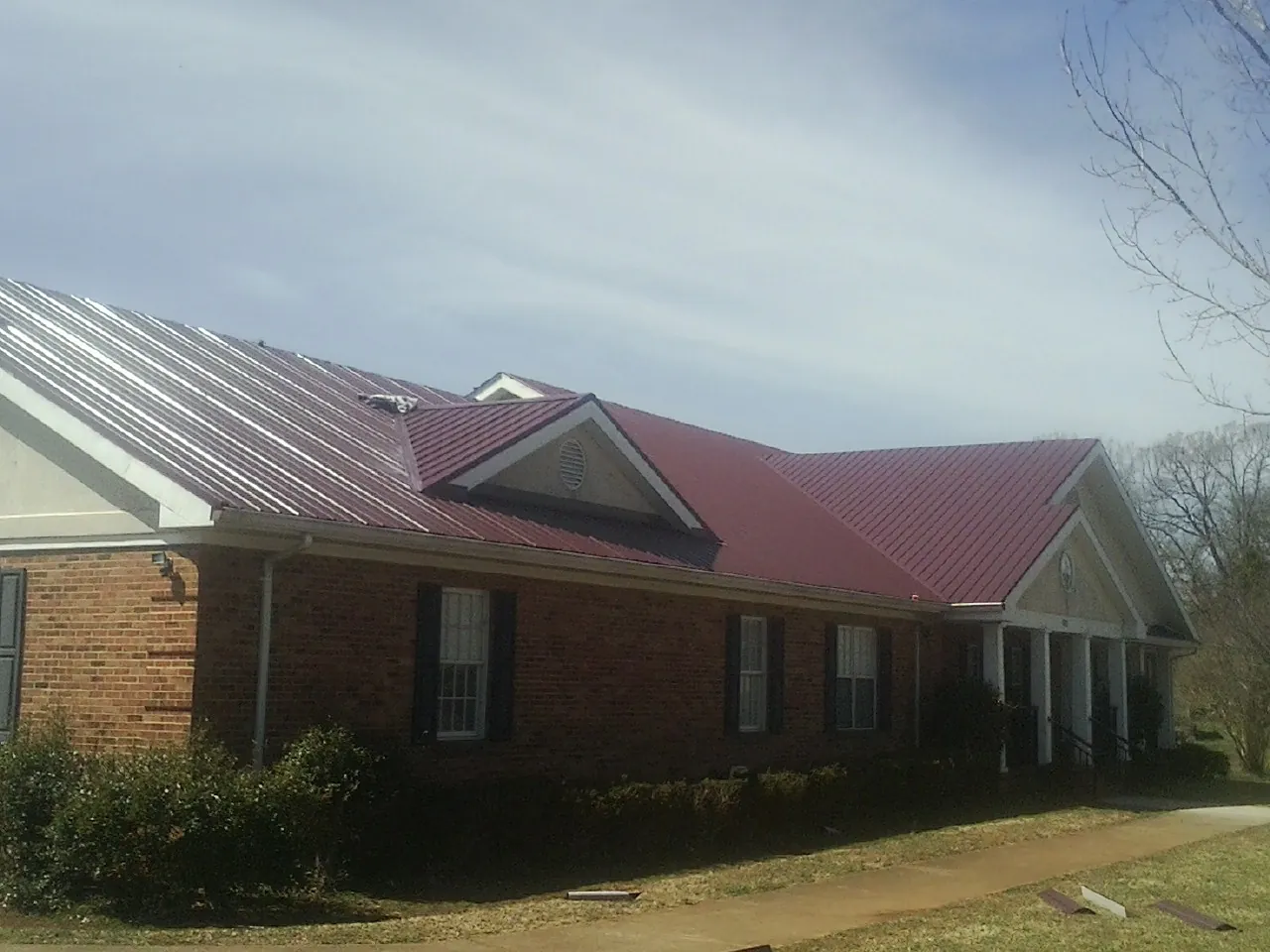 Red metal roof with gabled entries on a long brick building, from a Hail Damage Roof Repair job in Sturgis