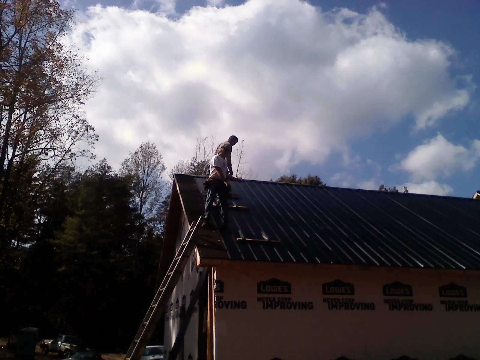 Roofer fastening dark metal panels high against a cloudy sky, from a Roof Inspection job in Sturgis