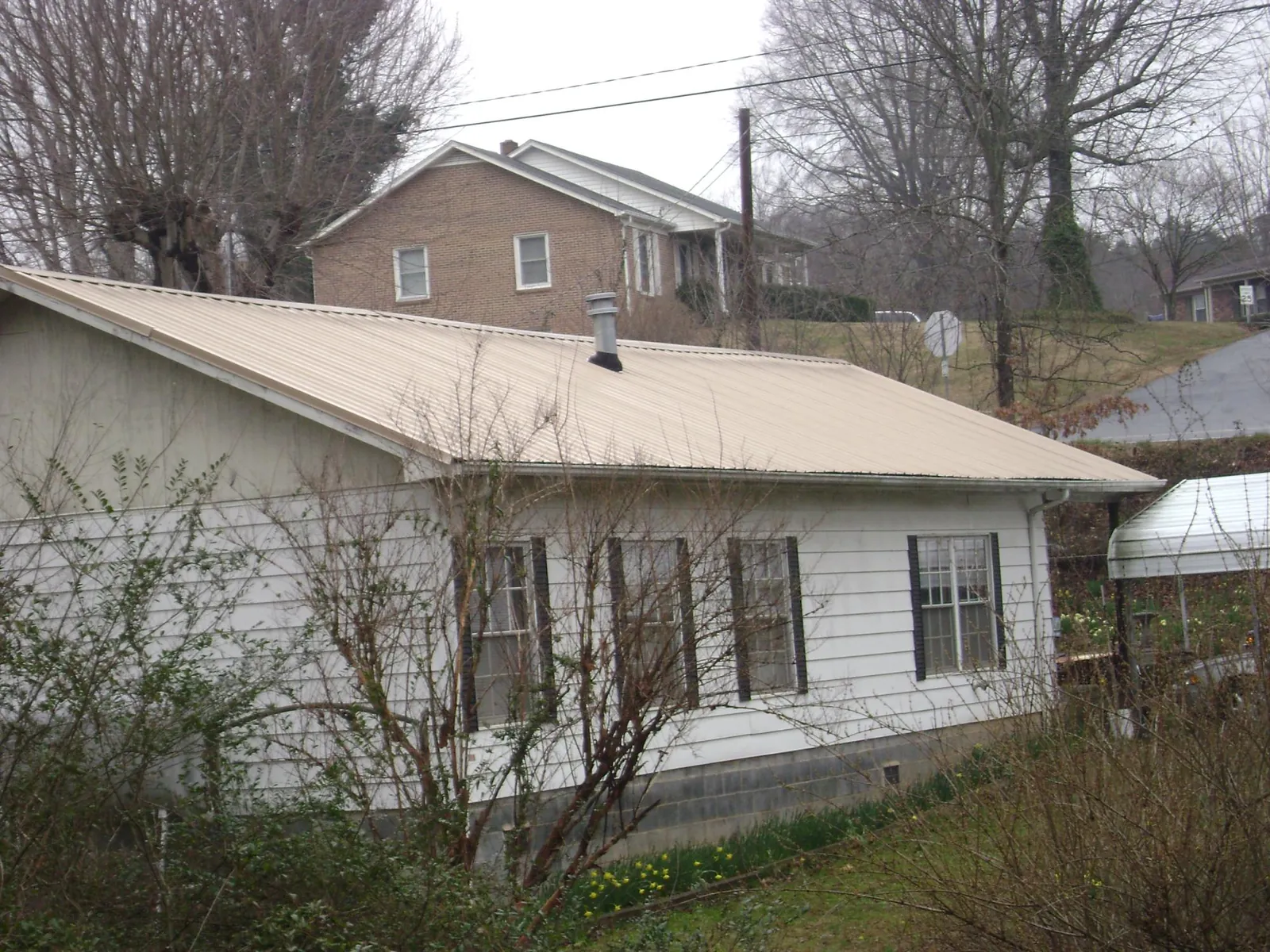 Tan metal roof on a white sided house set into a hillside — Commercial Roofing by Roofing Brothers in Sturgis